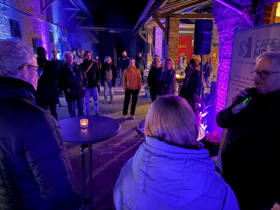 Menschen stehen abends in einem Hof bei violettem Licht.