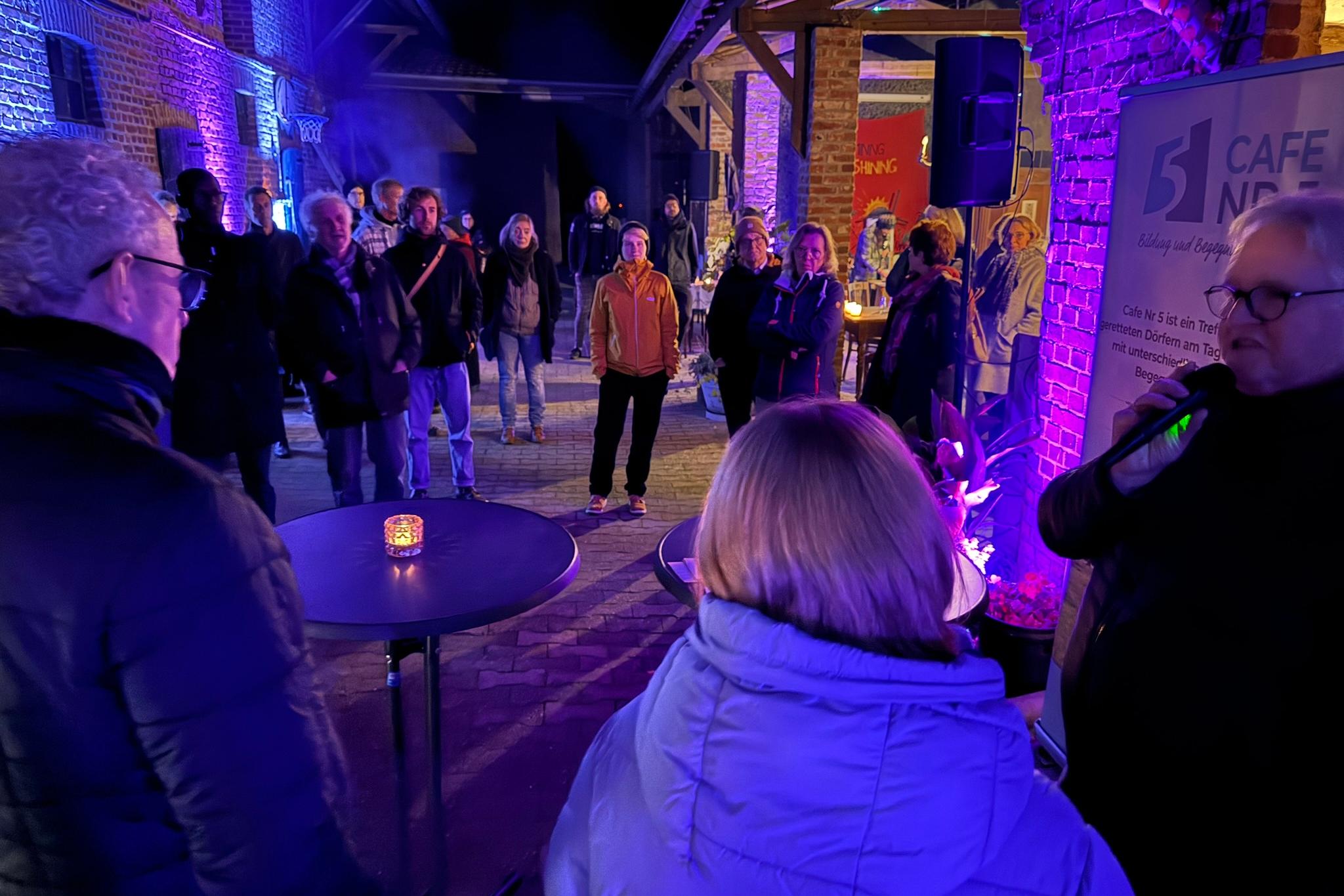 Menschen stehen abends in einem Hof bei violettem Licht.