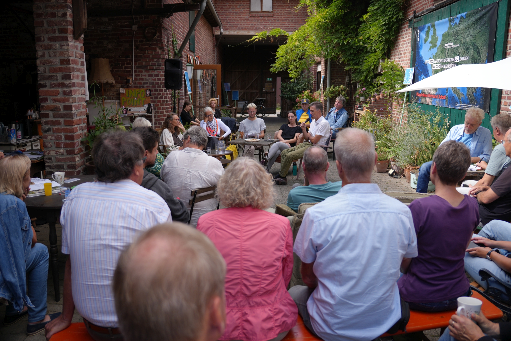 Menschen sitzen zusammen und schauen auf Menschen, die zu ihnen sprechen.