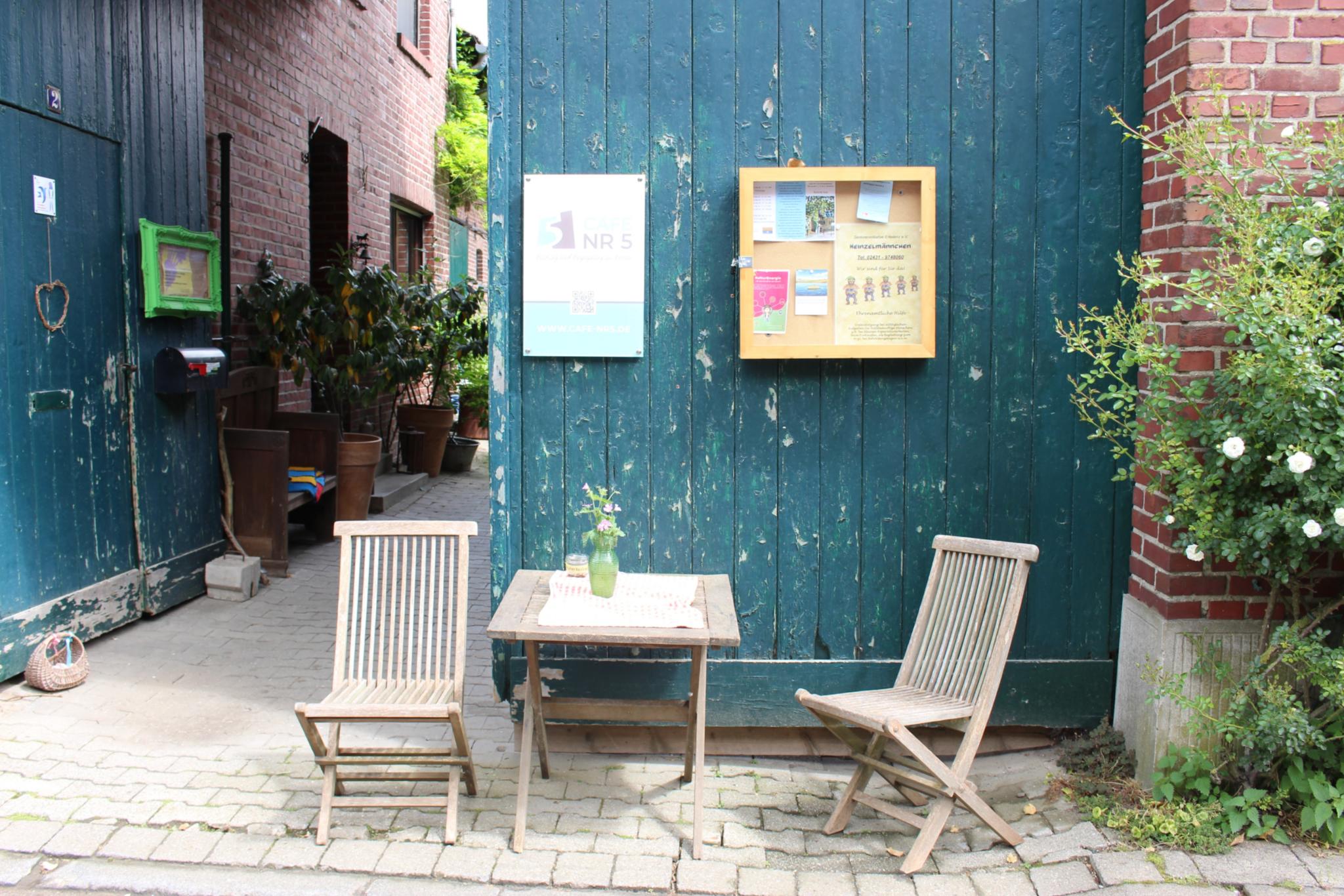 zwei stühle und ein Tisch vor einem grünen Holztor, schaukästen