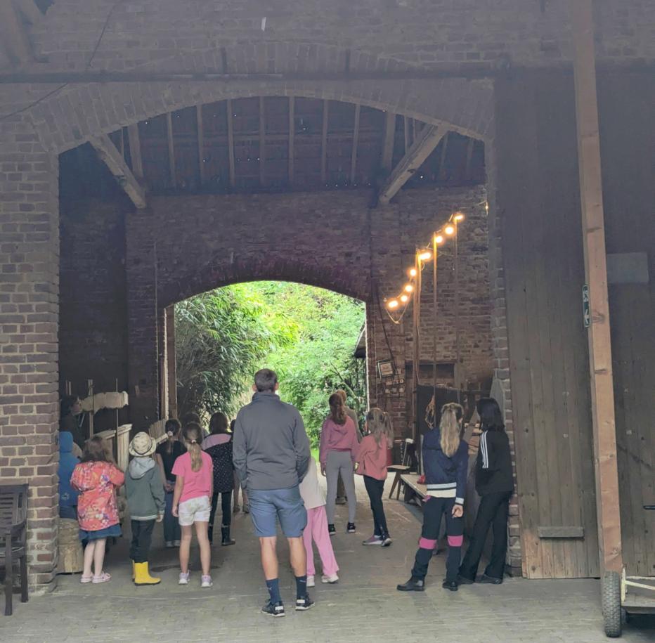 Gruppe von Kindern und einem Erwachsenen steht in einem großen, offenen Torbogen eines Backsteingebäudes mit Holzbalken und Lichterkette